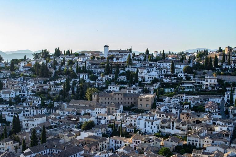 The white hillside of Granada’s Albayzín, with terracotta roofs, cypress trees and distant mountains.