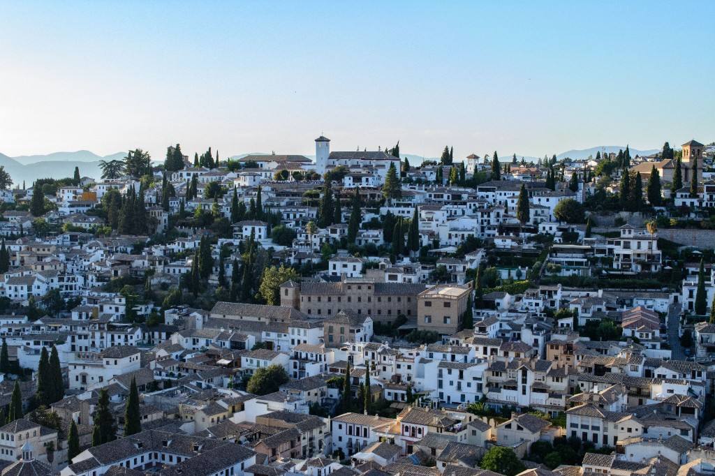 The white hillside of Granada’s Albayzín, with terracotta roofs, cypress trees and distant mountains.