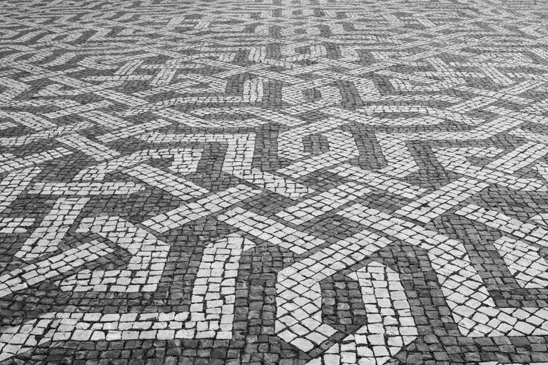 Close detail of Lisbon’s black-and-white calçada portuguesa, with interlocking geometric stone bands.