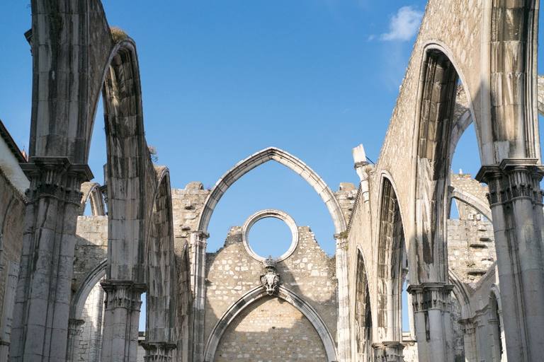 Open Gothic arches of the Carmo Convent in Lisbon, with columns framing blue sky where the roof once was.