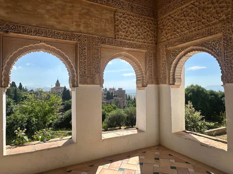 Three ornate Nasrid arches opening onto Granada, with the Alhambra visible through the centre span.