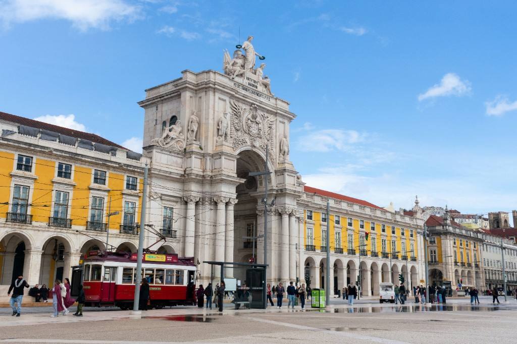 A red tram in Praça do Comércio before the Rua Augusta Arch and the arcaded yellow façades.