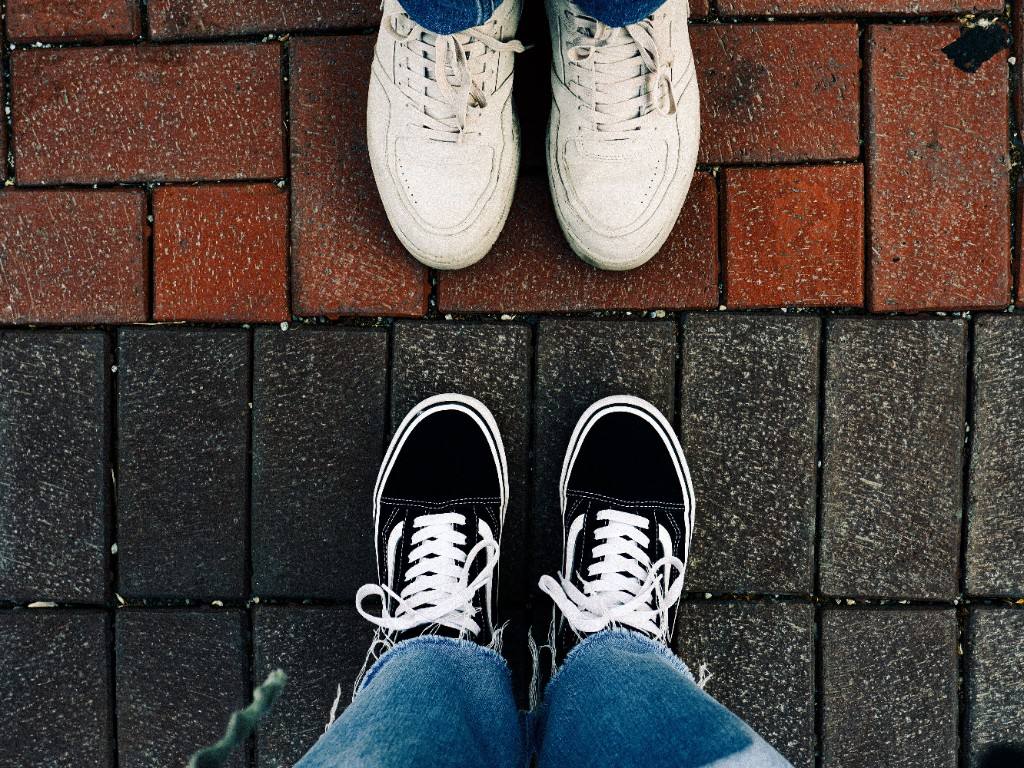Two pairs of feet facing each other on a pavement split between reddish and dark grey stones.